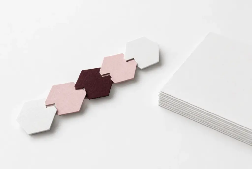 Chain of hexagonal paper tiles in white, blush and burgundy beside a stack of sheets