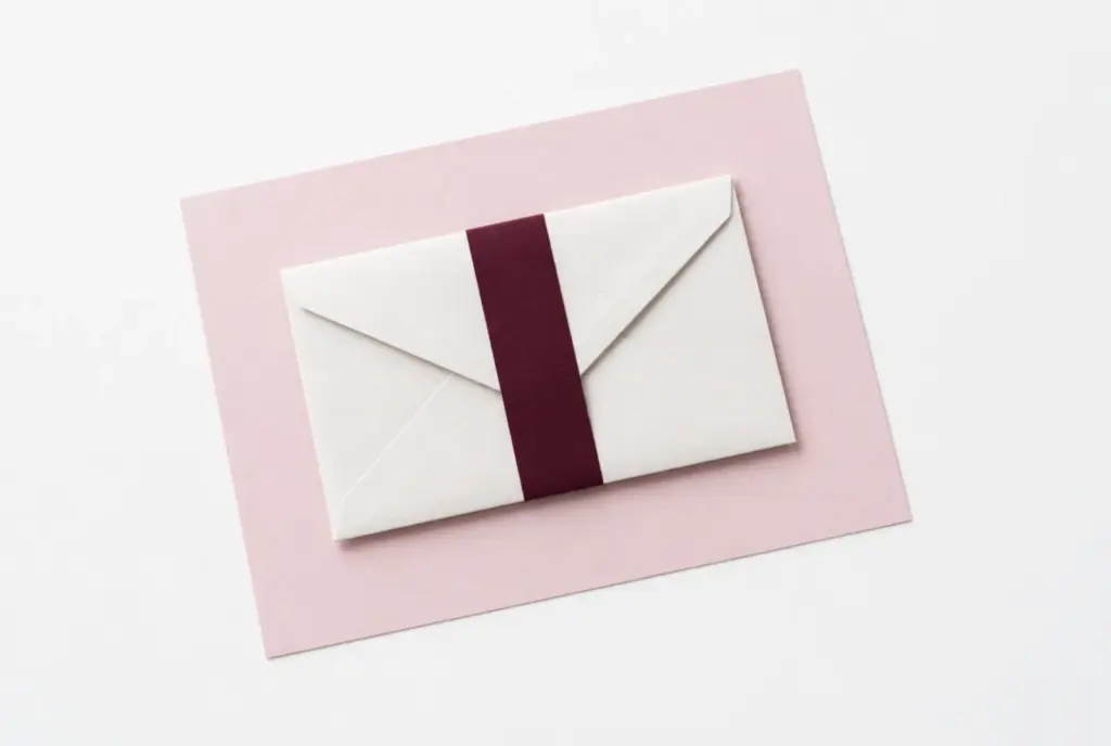 Closed paper envelope held by a burgundy band on a blush sheet