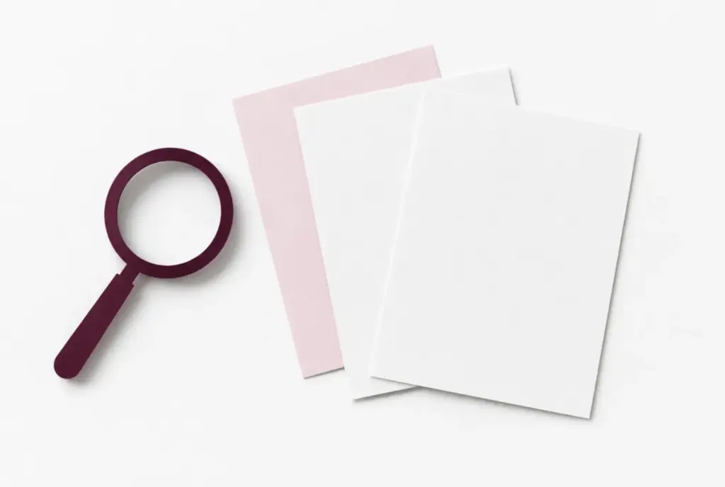 Paper magnifying lens beside blank white and blush sheets